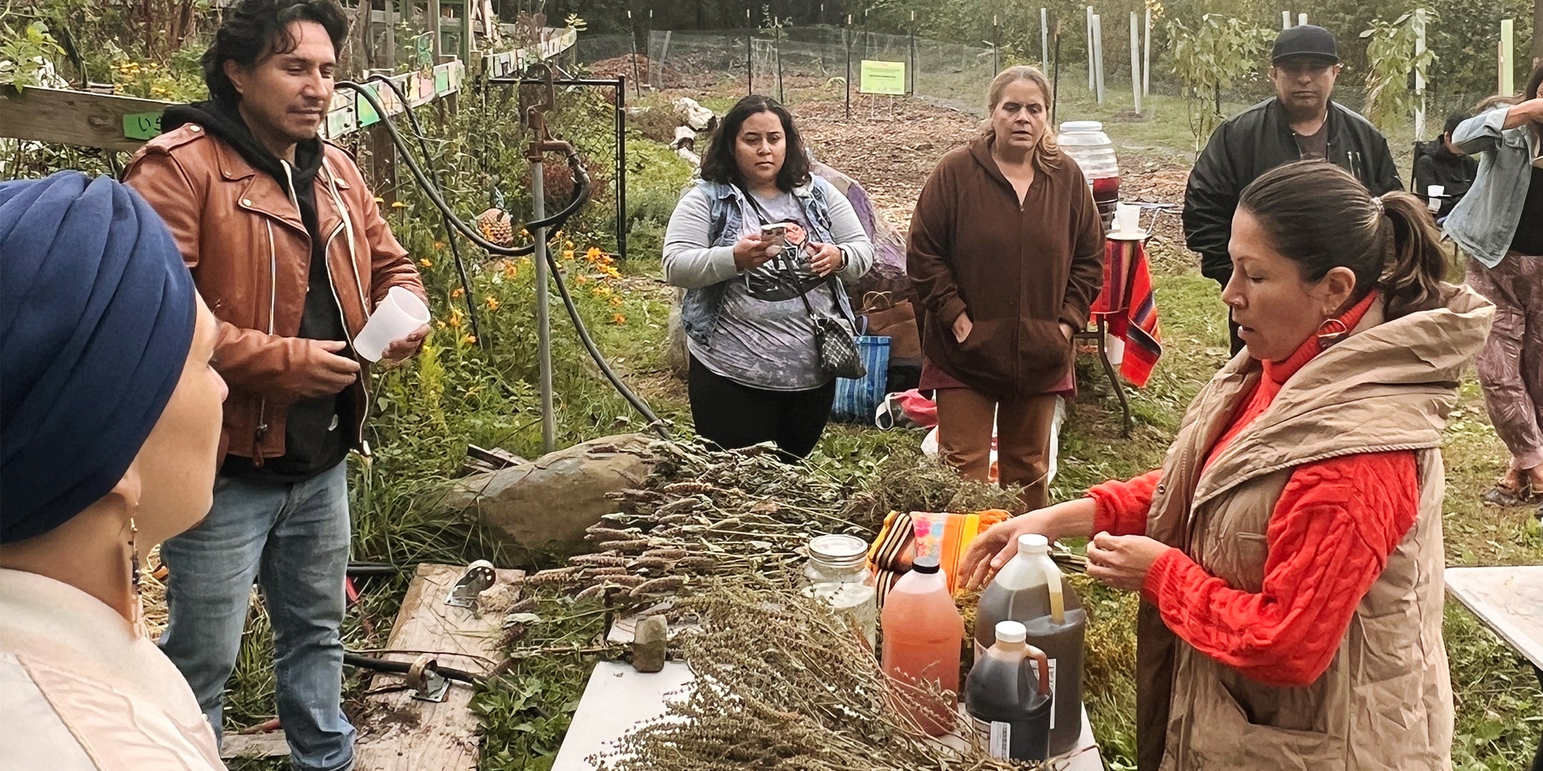 Group of people in an outdoor setting, possibly a market or community event, with various items on display.