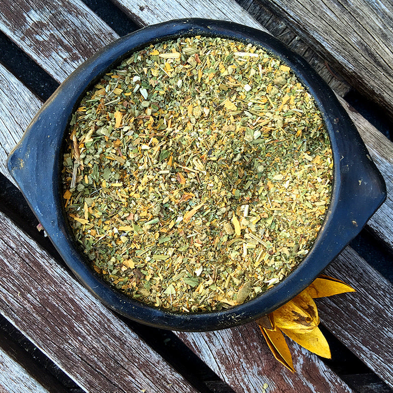 Blend of green herbs in black ceramic bowl on wood panels – FOCUS herbal mix