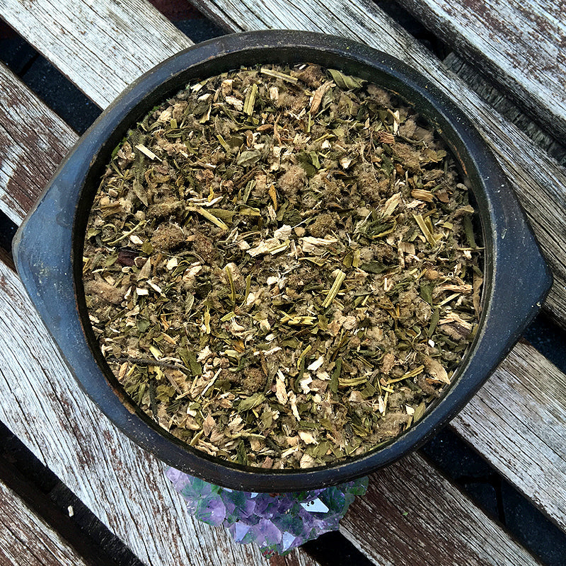 Herbal mixture in a black bowl on a wooden surface