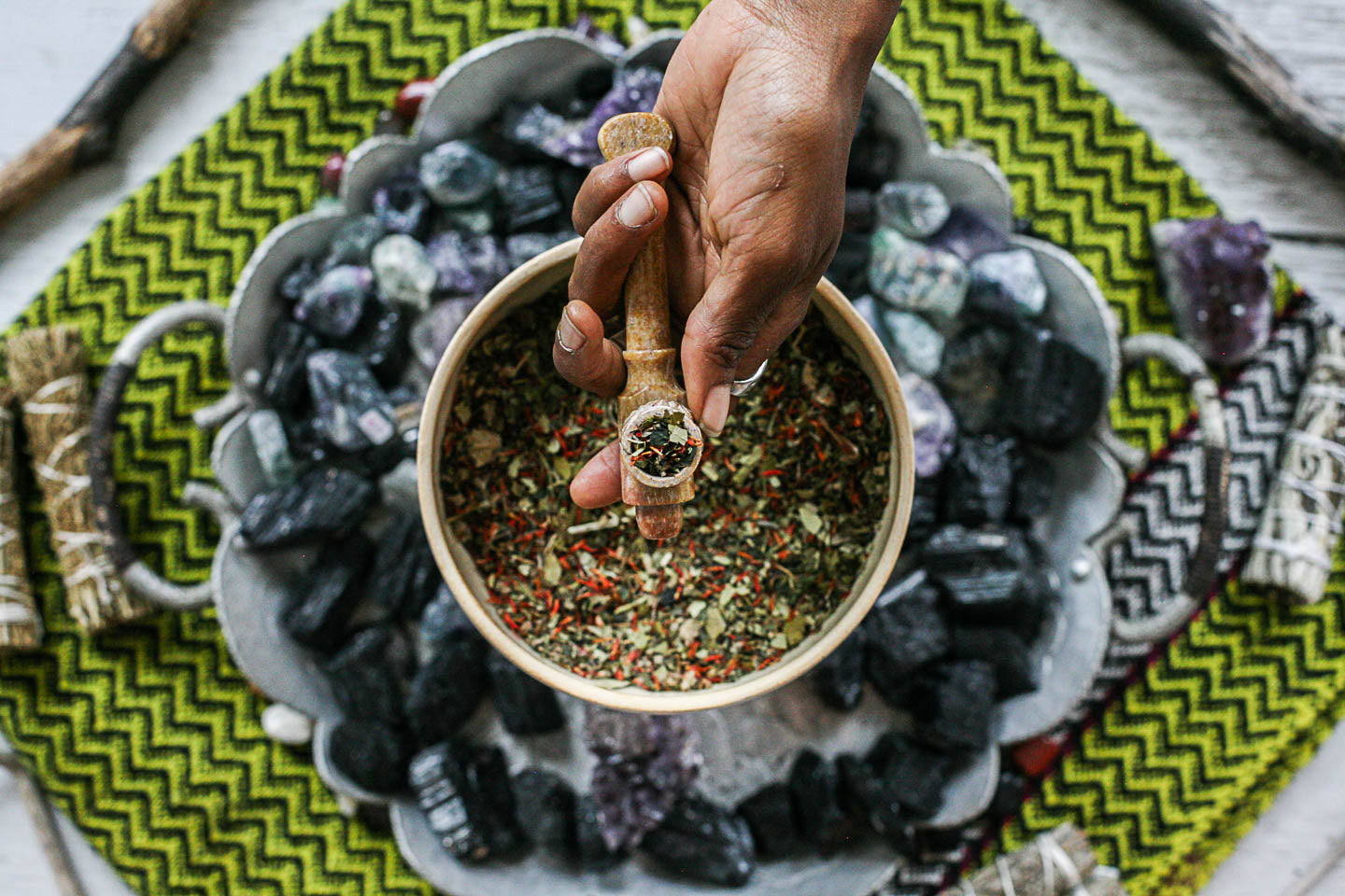 Hand holding a small container over a bowl of spices on a decorative stone surface with crystals.