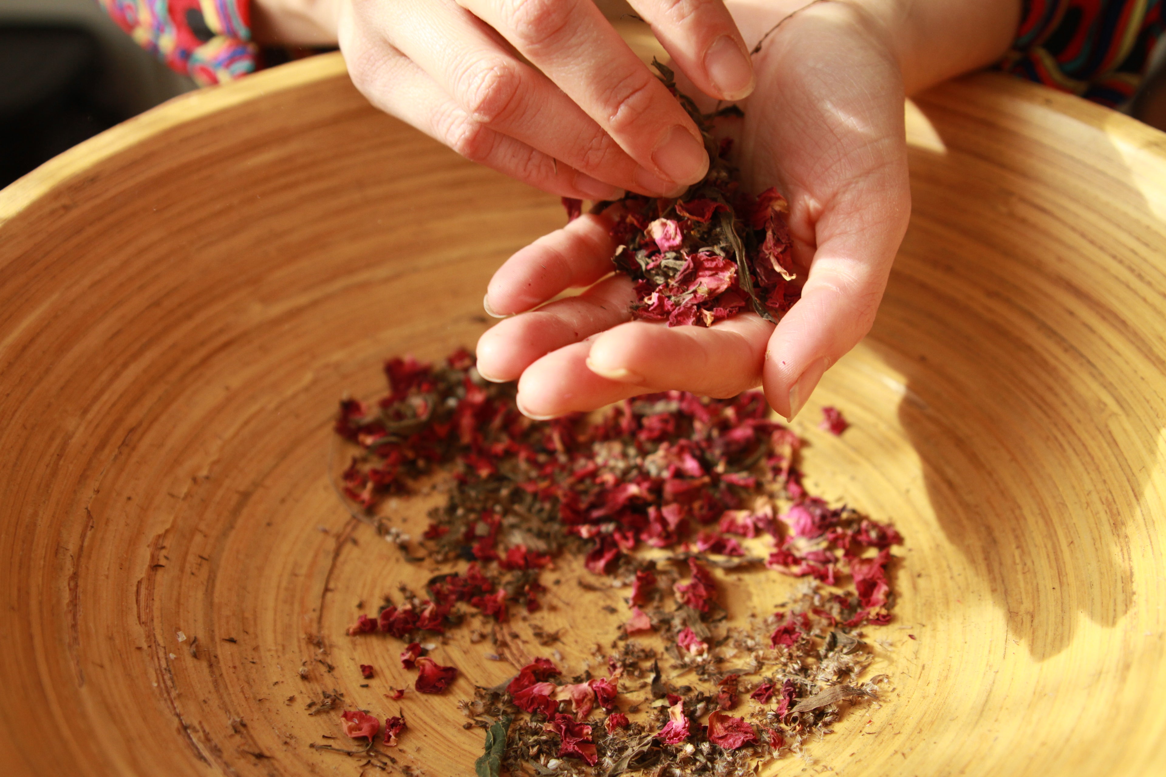 Hands holding dried flowers over a wooden bowl