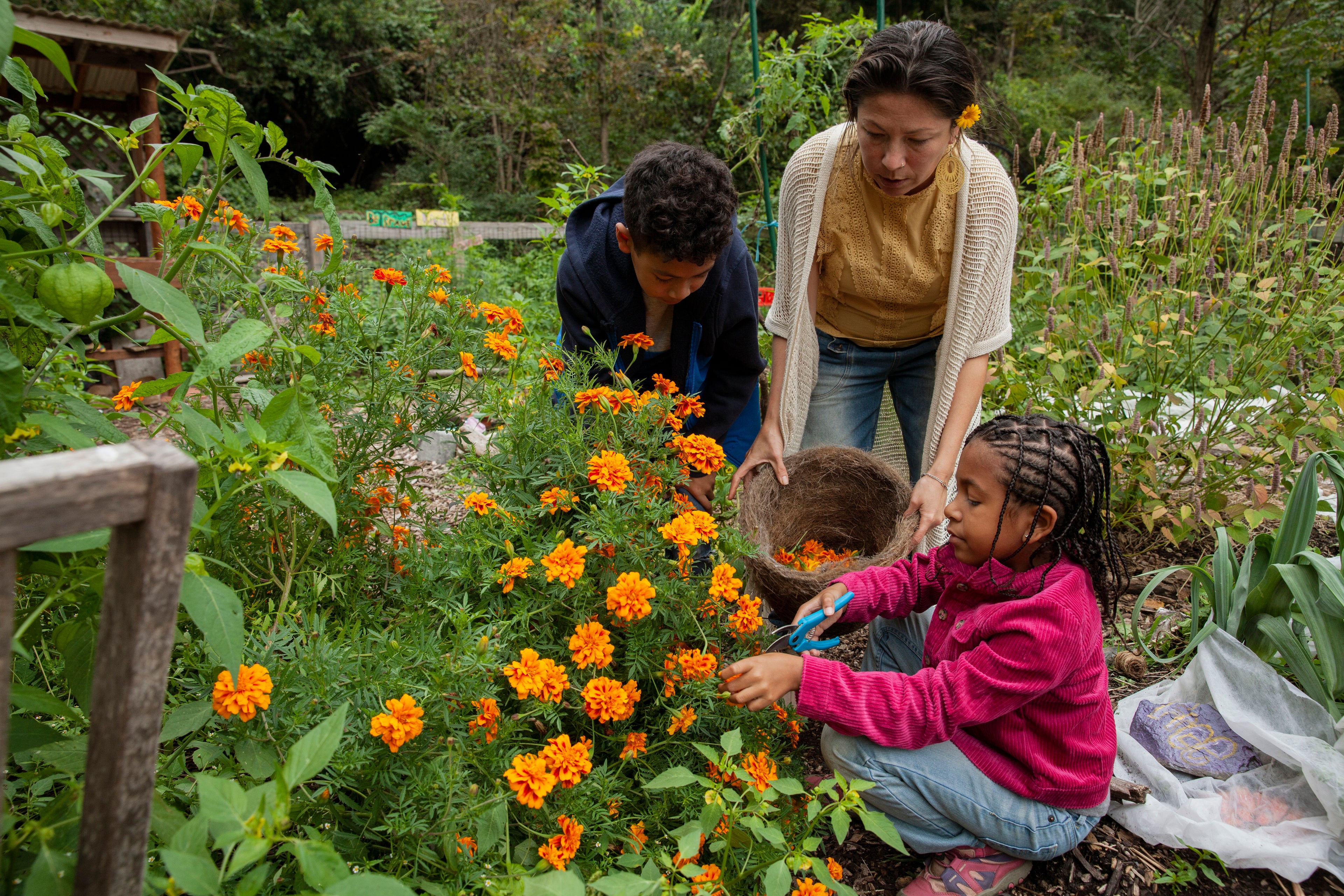 Family of three, including a woman and two children, tending to flowers in a garden.