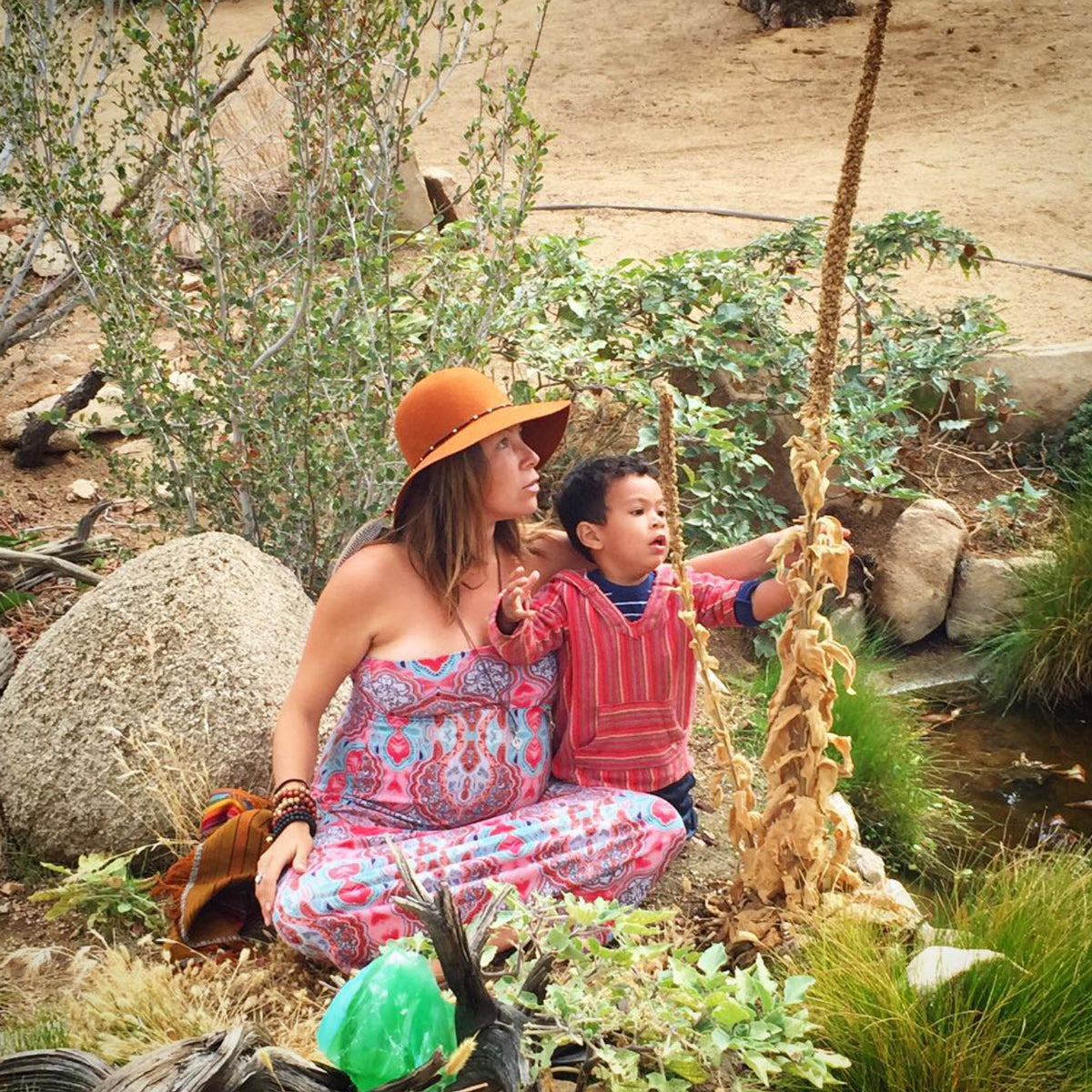 Woman and child sitting on a swing in a natural setting with rocks and plants.