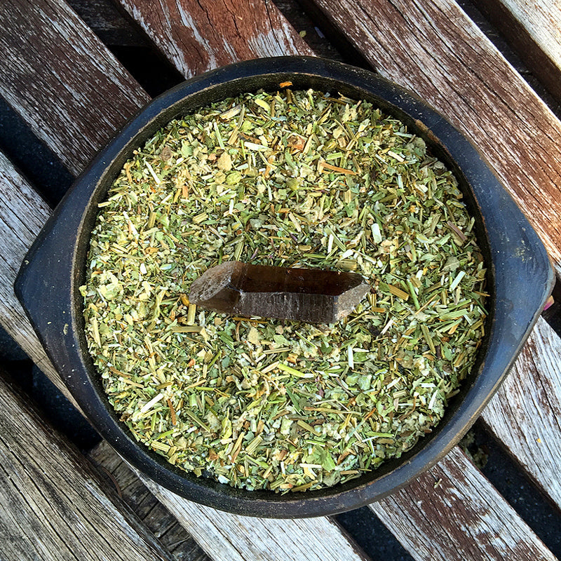 Smoky quartz crystal placed in a bowl of QUIT herbal blend on wood surface