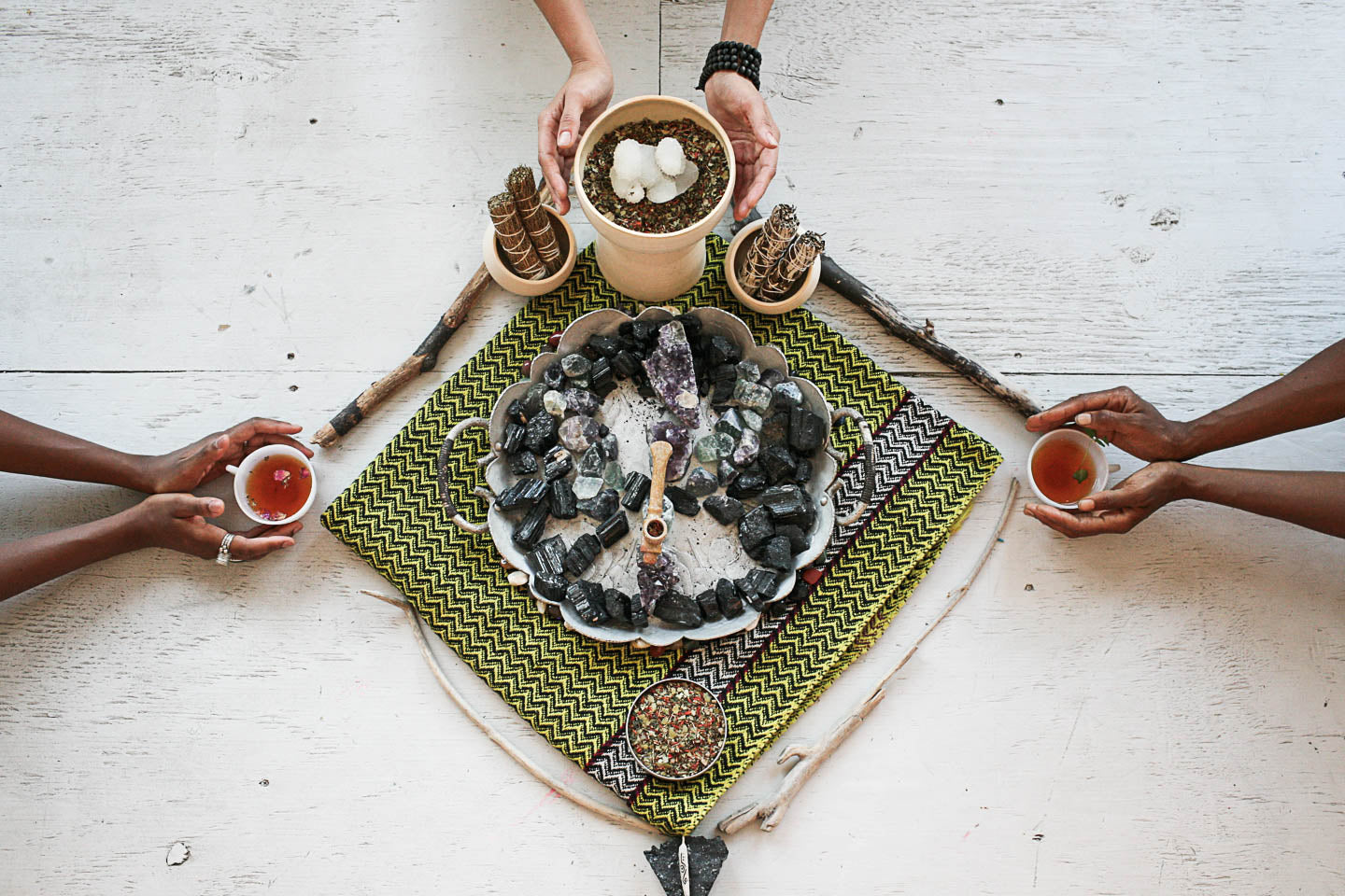 Three people holding cups around a small garden setup on a white wooden surface.