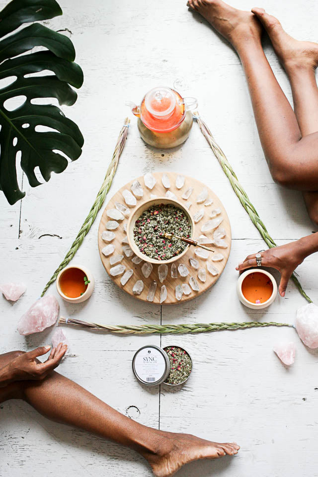 Relaxing scene with a bowl of herbs, cups, and a plant on a white surface.