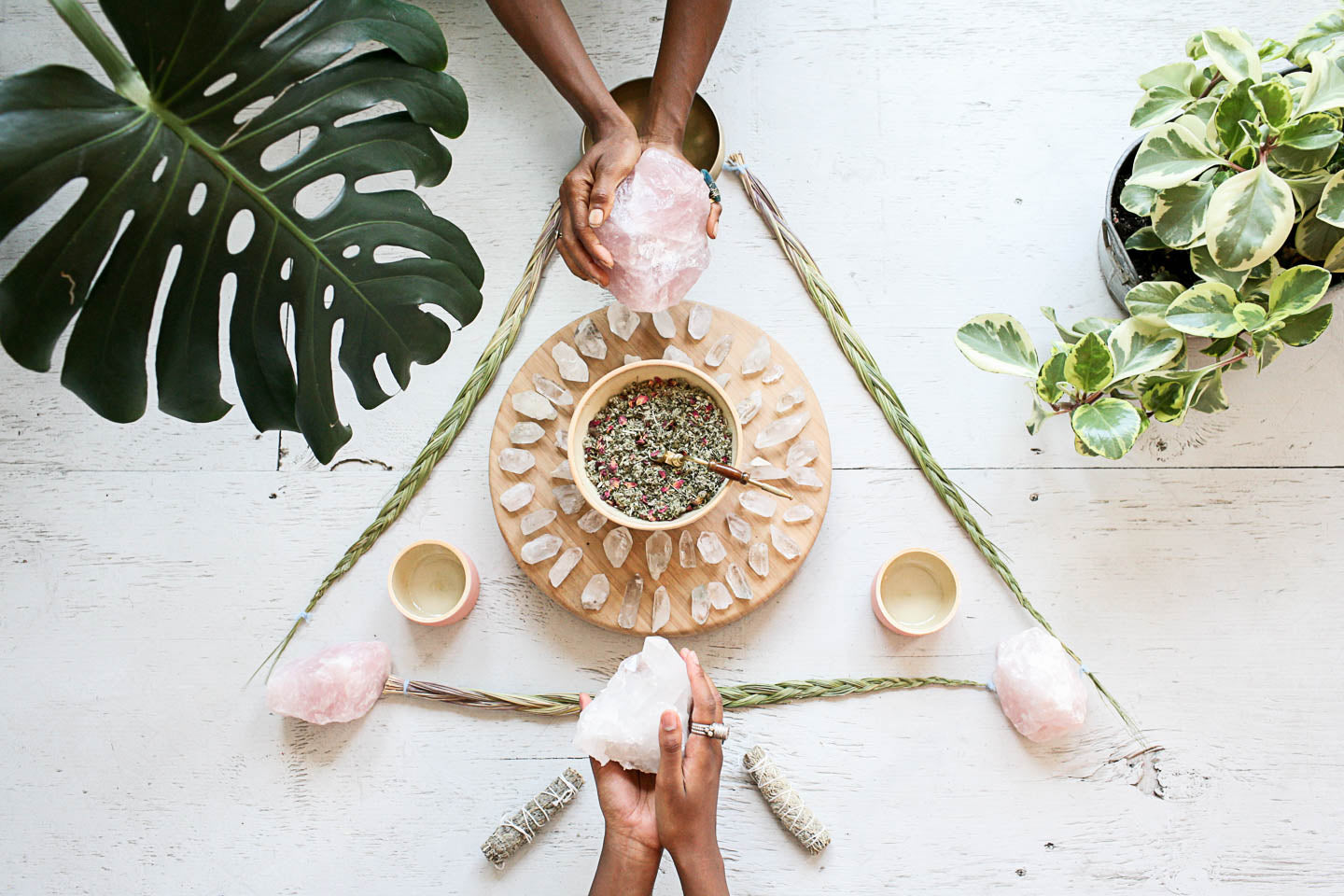 Two hands holding rose crystals over a triangle alter of sweet grass.