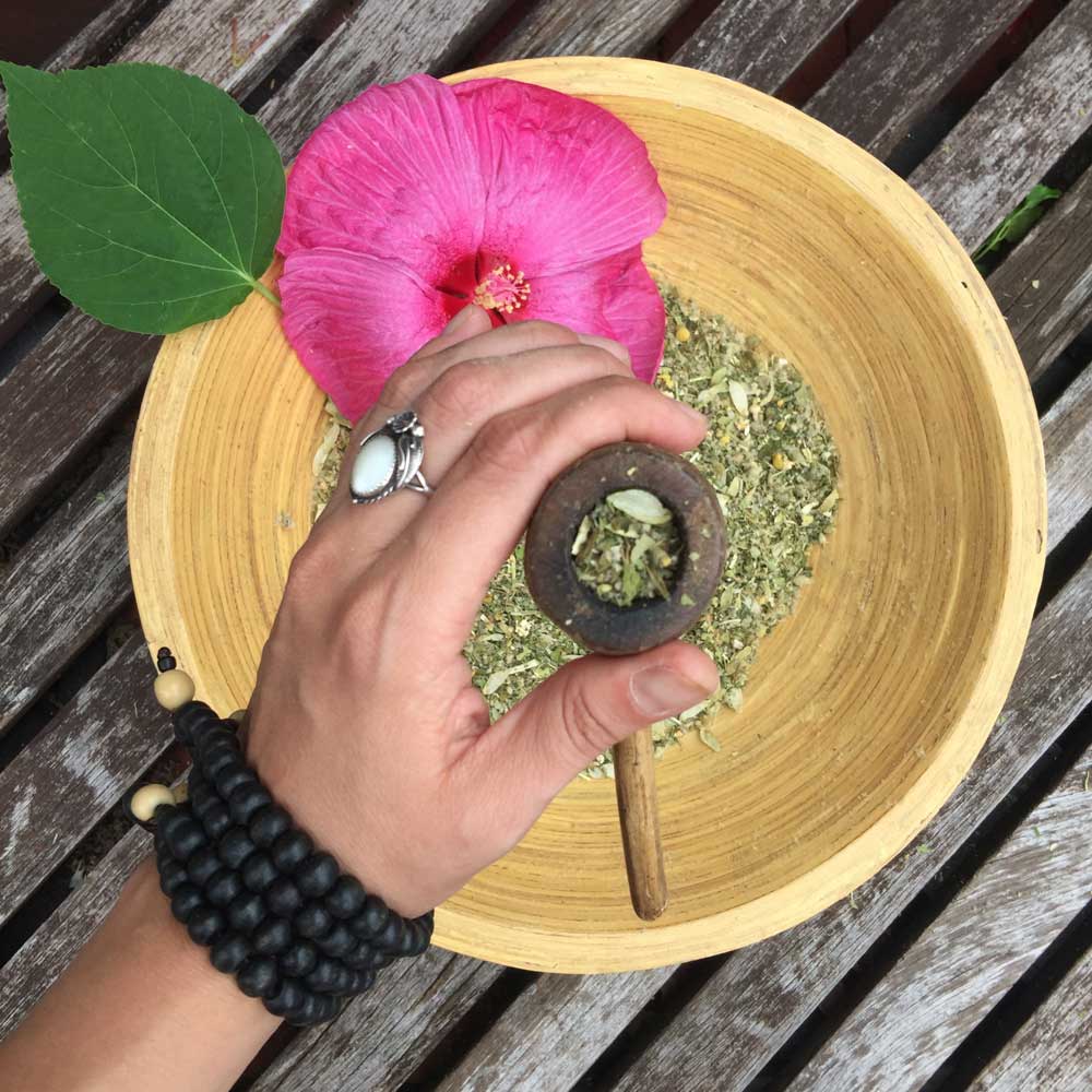 Female Hand holding pipe above bowl of herbal blends and MOON flower