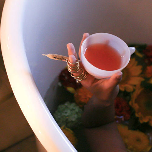 Hand holding tea and herbal preroll in a bath